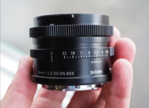 Ультракомпактный объектив Sigma 45mm f/2.8 DG DN Contemporary в руке фотографа: видны механическое кольцо диафрагмы с засечками и фрезерованные металлические насечки на кольцах управления